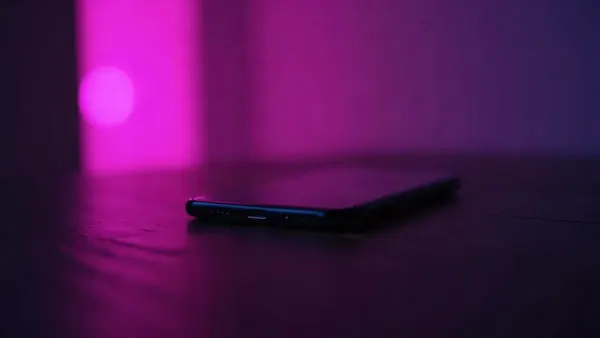 Smartfon na ciemnym drewnianym stole, otoczony fioletowymi i różowymi refleksami (ilustracja do artykułu)